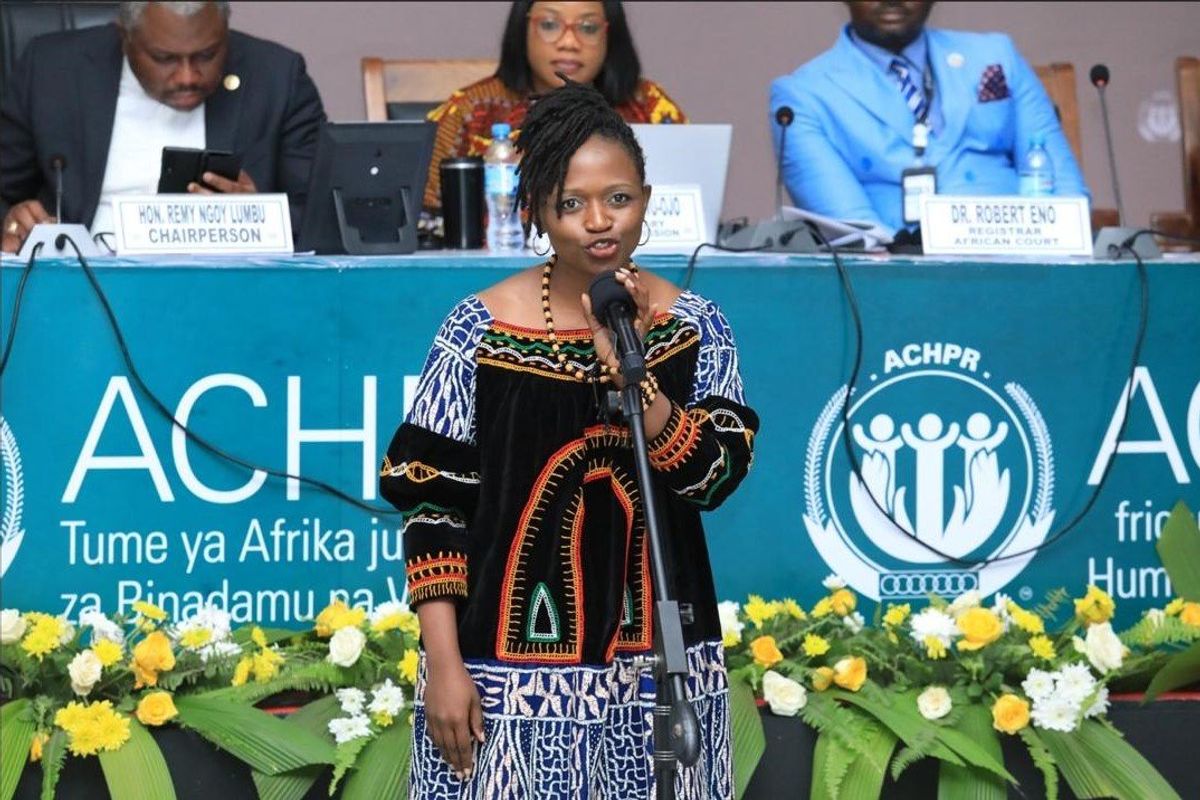 A woman in traditional dress stands at a microphone at an official looking event. 