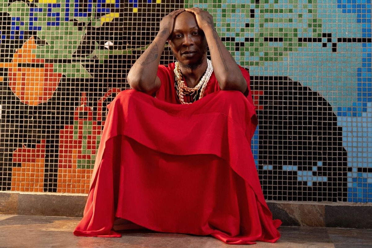 Afrobeat icon Seun Kuti sits with his hand on his head, wearing red.