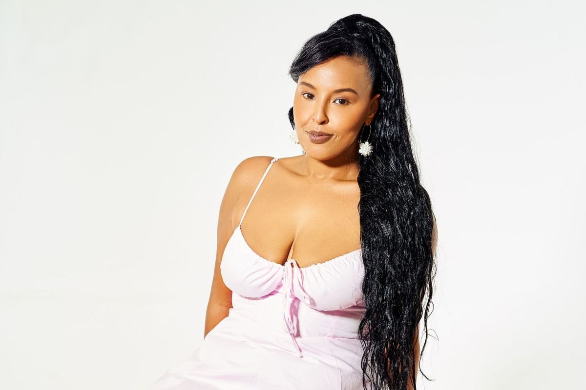 Faiza Hersi poses in a soft pink dress, sitting on a white block against a white background
