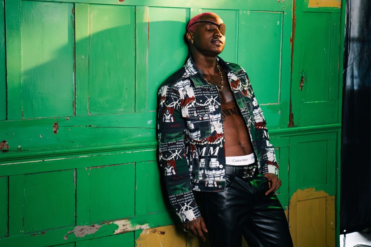Ruger poses in a colorful jacket against a green background 