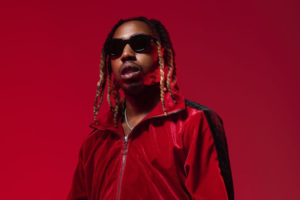 South African rapper 25K poses in a red tracksuit and sunglasses in front of a red backdrop.