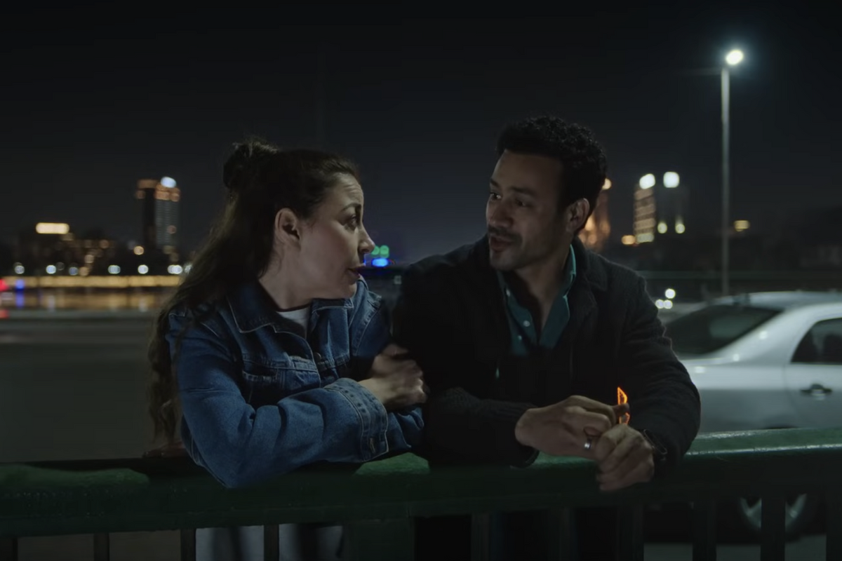 A still from ‘El Hawa Sultan’ showing Menna Shalaby and Ahmed Dawood speaking together while resting on the green railings of a bridge. 